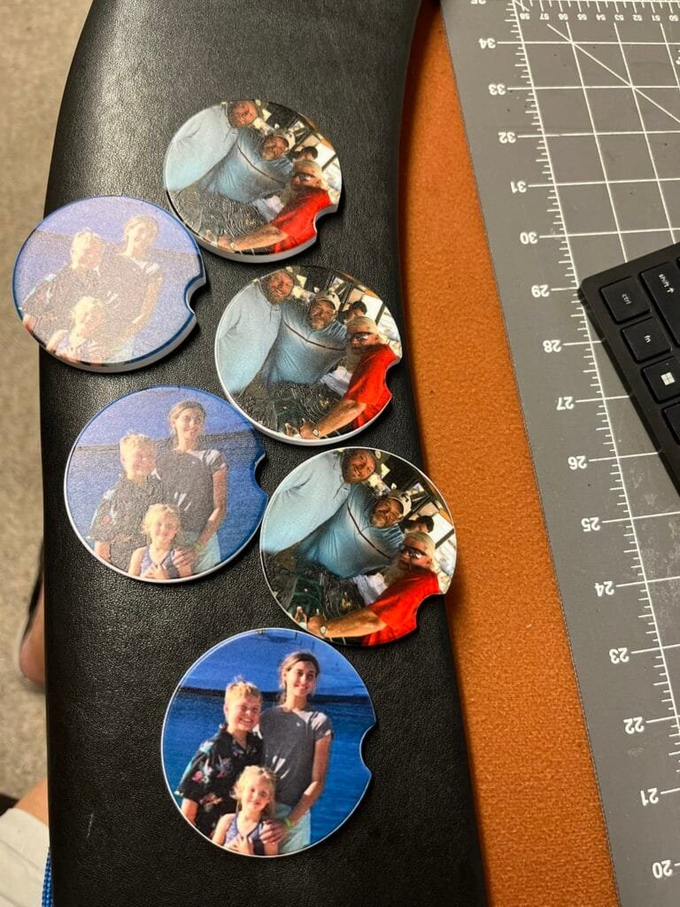 Circular photo pins showing group pictures of people posing together, placed on a black surface near a cutting mat and ruler pieces.