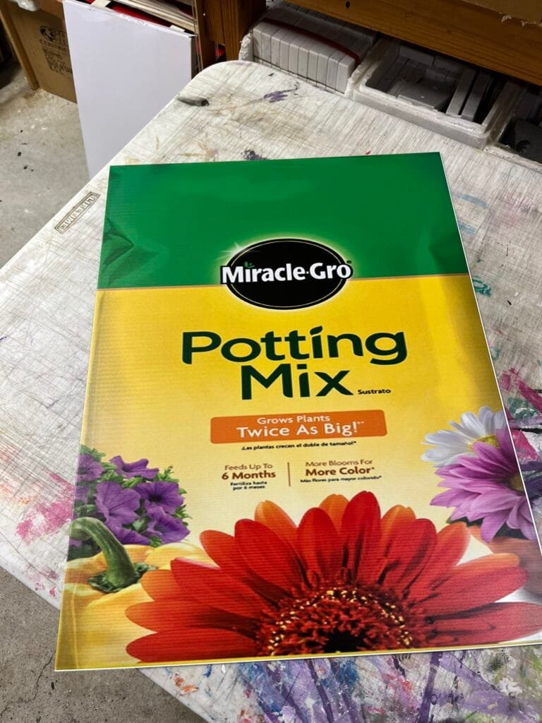 Miracle-Gro Potting Mix bag on a paint-splattered workshop table in storage area.