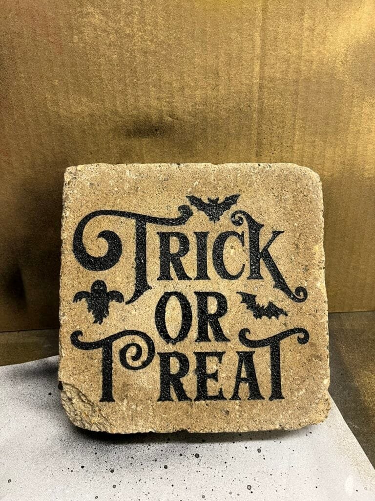 Close-up of a textured stone tile with black ornate lettering, showing partial words.