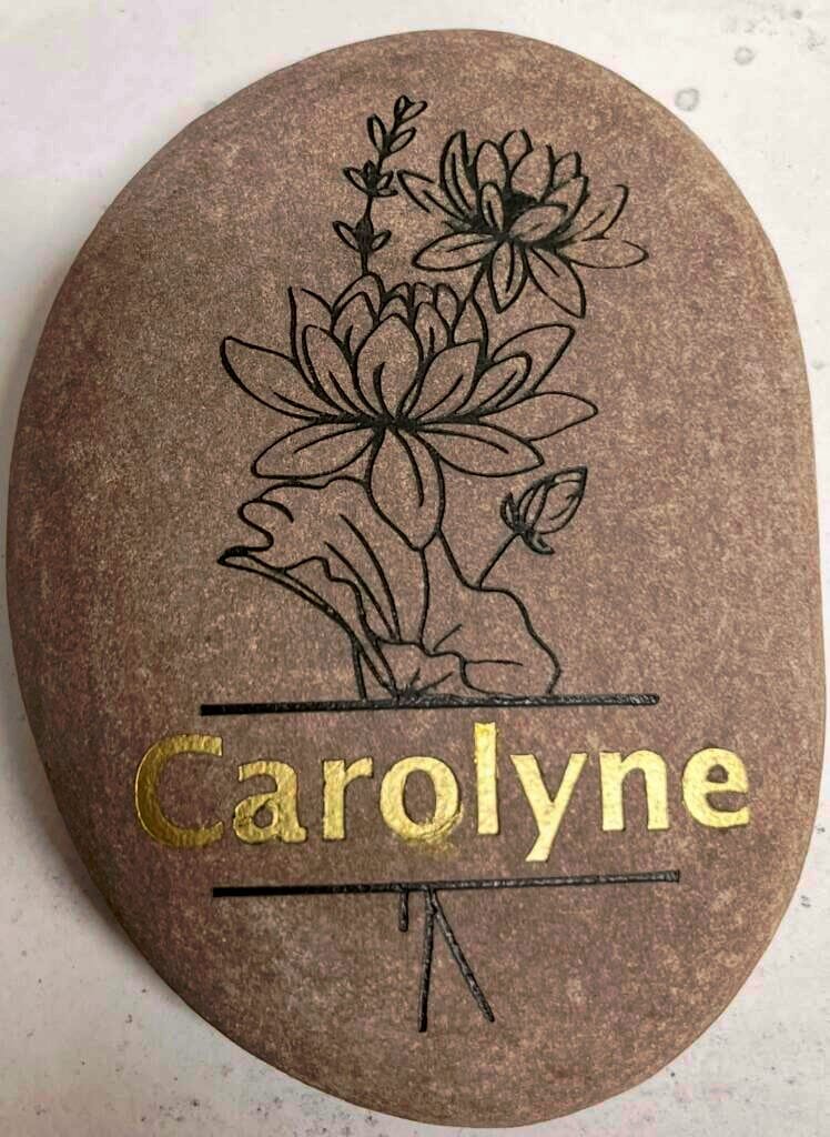 Oval stone plaque featuring a black line drawing of a blooming bouquet above the gold name Caroline.