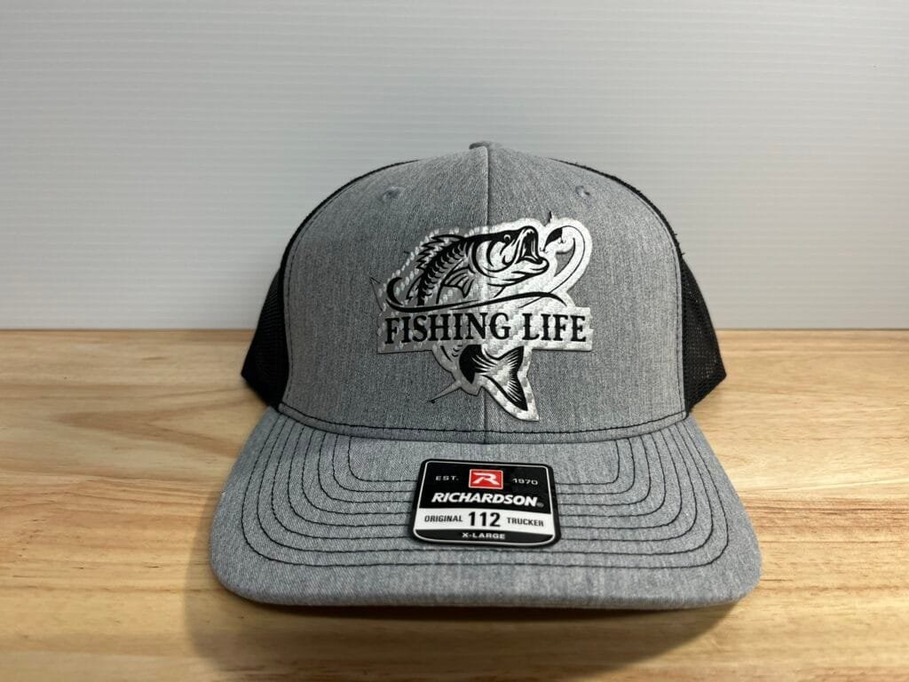 Gray Richardson fishing life trucker hat with a large fish logo on a wooden surface, front view.