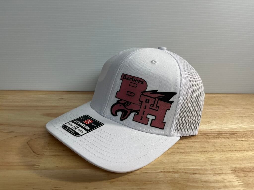 White trucker-style cap with a red graphic design on the front, placed on a wooden table against a gray wall.