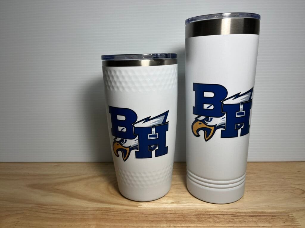 Two white insulated tumblers with blue graphic and eagle logo, topped with silver lids, on a wooden surface.