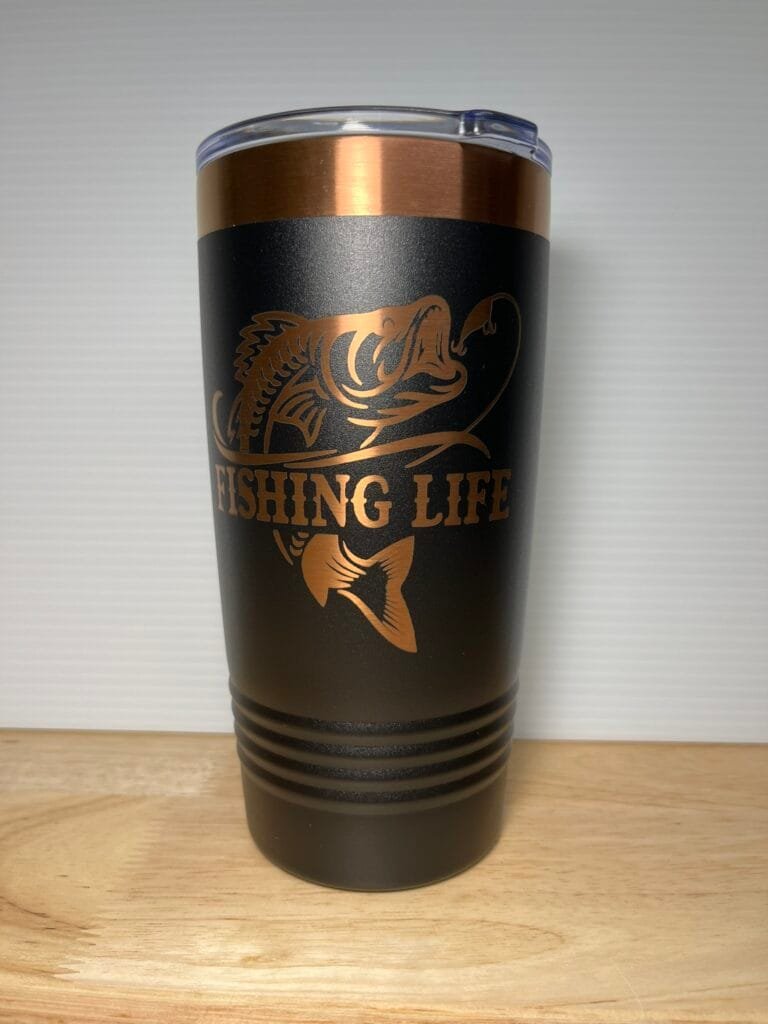 Black tumbler with copper band and gold 'FISHING LIFE' logo featuring a fish graphic, on a wooden surface.